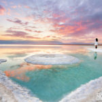 woman standing on salt flats watching the sunrise at the dead sea in israel