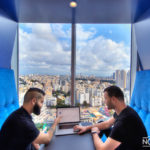 two workers with a laptop in the office with city views