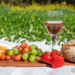 outdoor picnic on the grass with glass of wine, fruits, cheese and bread